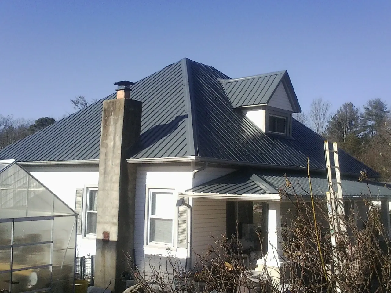 Dark blue standing seam metal roof on a white farmhouse with dormer — Slate & Tile Roof Repair by Roofing Brothers in Meadow Valley
