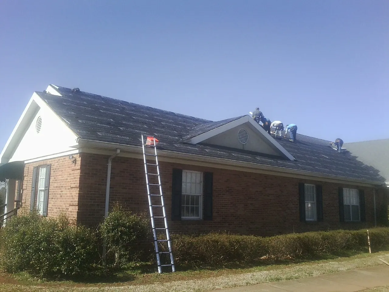 Crew tearing shingles off a brick ranch roof with a ladder set — Emergency Roof Repair work by our crew in Meadow Valley