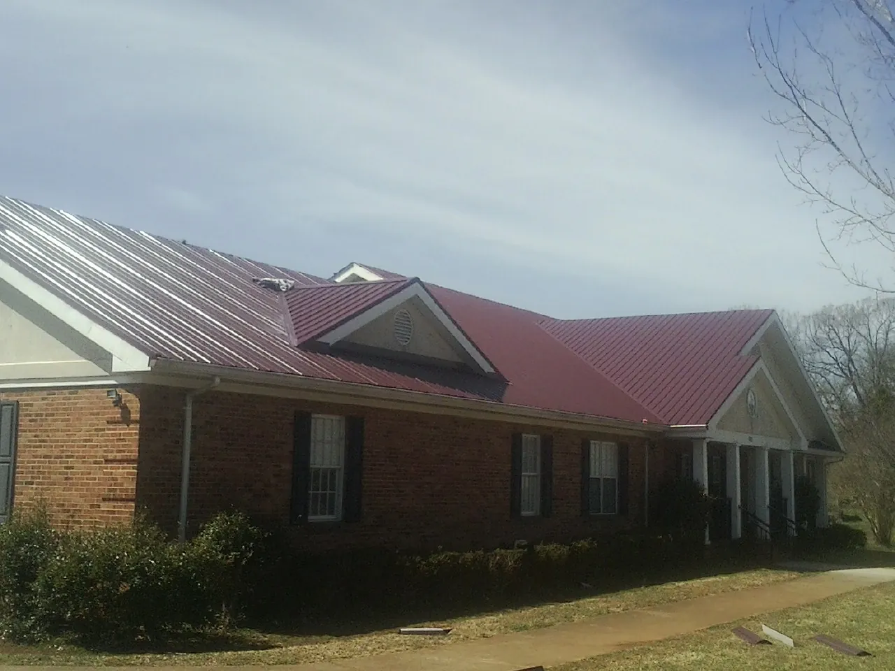 Red metal roof with gabled entries on a long brick building, from a Hail Damage Roof Repair job in Meadow Valley