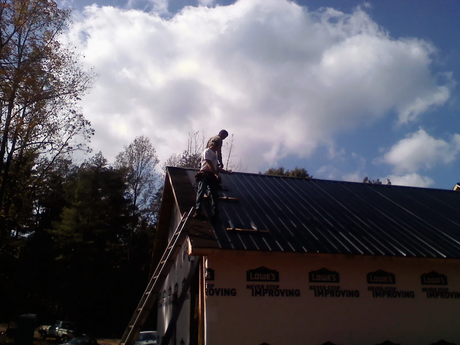 Roofer fastening dark metal panels high against a cloudy sky, from a Roof Inspection job in Meadow Valley
