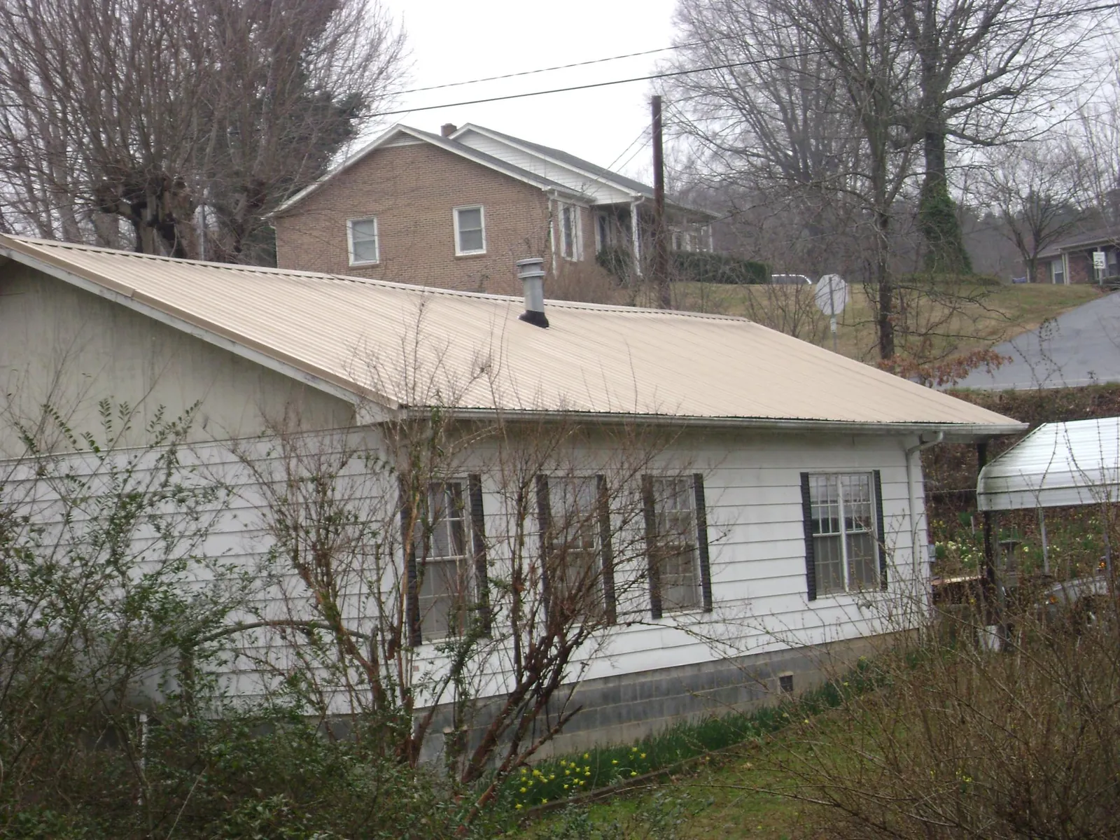 Tan metal roof on a white sided house set into a hillside — Commercial Roofing by Roofing Brothers in Meadow Valley